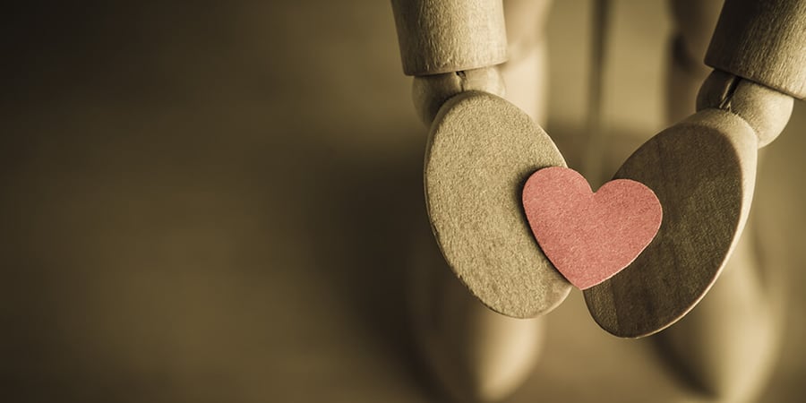 A wooden hand holding out a heart, representing the love between inbound and paid advertising